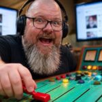 Thor Jadesø ved et farverigt mixerbord med høretelefoner på, der begejstret skruer op for en knap, som om han styrer algoritmen