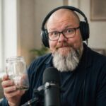 Thor Jadesø med store studiehøretelefoner holder et glas med mønter op ved sin mikrofon og kigger overrasket ind i kameraet