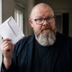 Thor Jadesø står ved postkassen i gangen, holder en åbnet kuvert op og ser skeptisk ind i kameraet