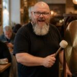 Thor Jadesø slår på en stor messinggong på en café, så gæsterne kigger overrasket op fra deres telefoner