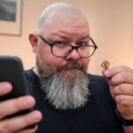 Thor Jadesø kigger skeptisk på sin telefon med en lille nøgle i den anden hånd, klar til at låse døren